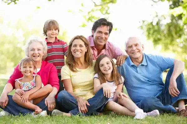 Grandparents, parents, and children sitting together on the grass outdoors, enjoying quality time as an extended family.