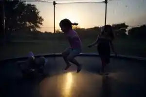 Children playing on a backyard trampoline at dusk.