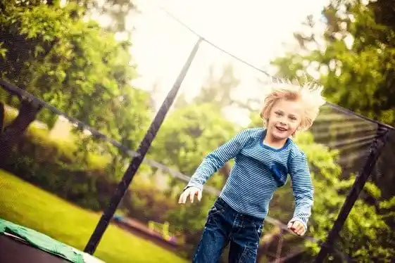 Young child smiling while jumping on a backyard trampoline with a safety enclosure net.