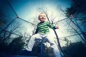 Young child smiling while bouncing on a backyard trampoline enclosed by a safety net, enjoying outdoor play.