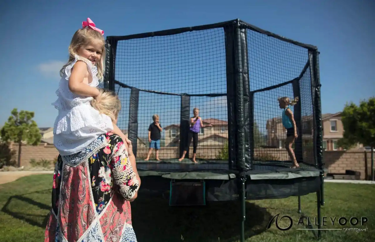 A girl on her mom's shoulders in front of an AlleyOOP trampoline. 