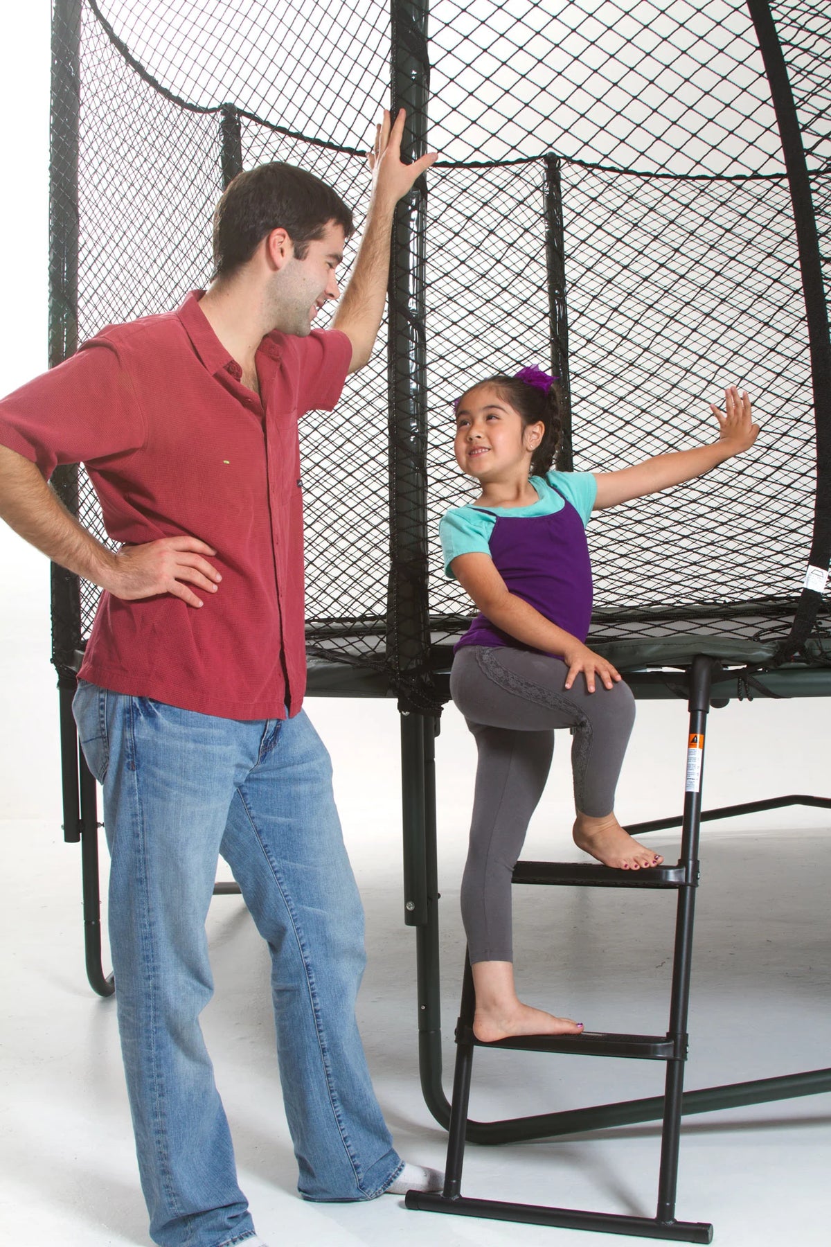 Child using a JumpSport trampoline ladder to climb onto the trampoline with an adult standing nearby.